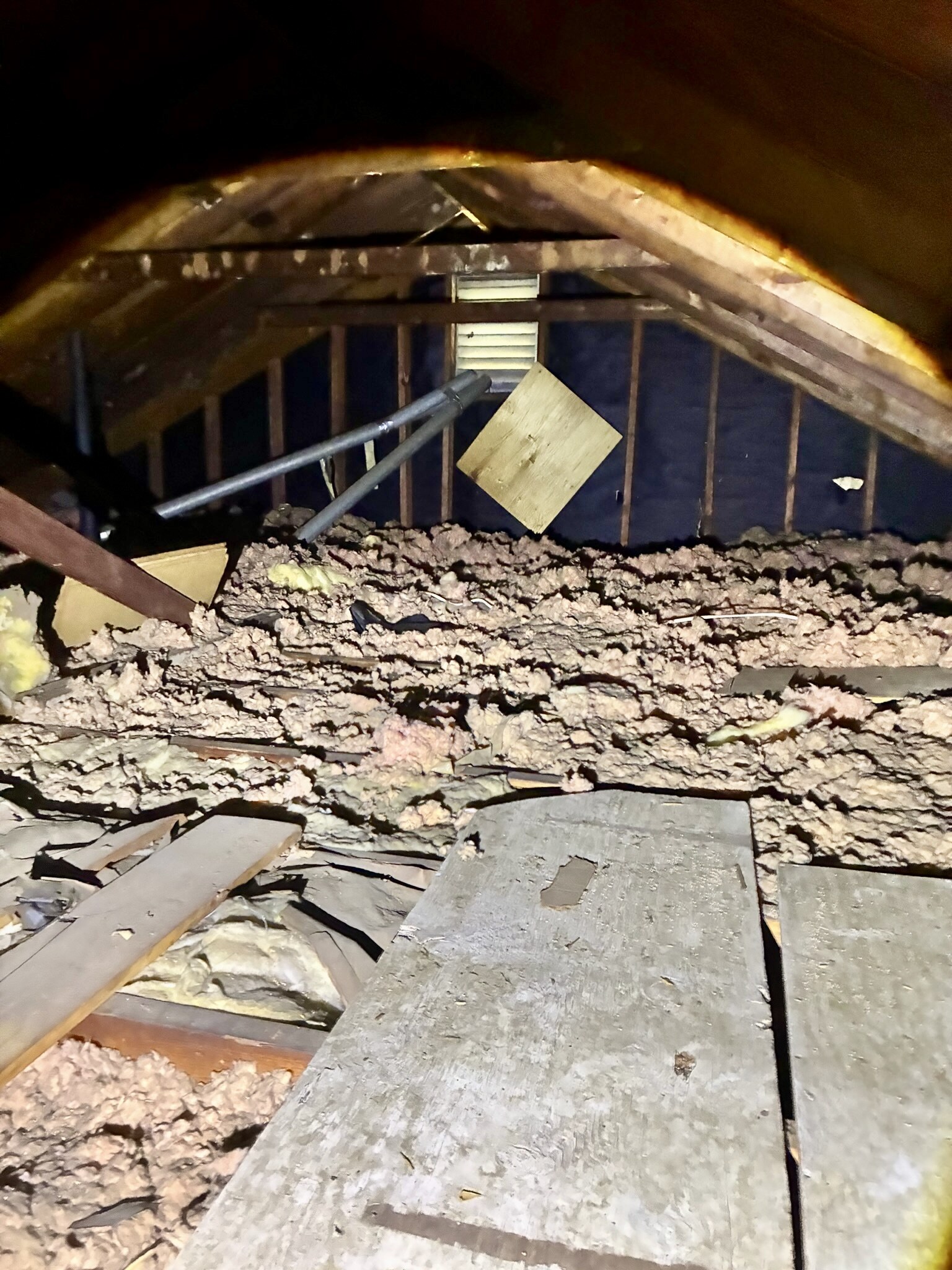Older attic insulation before replacement with uneven darkened material and exposed attic decking